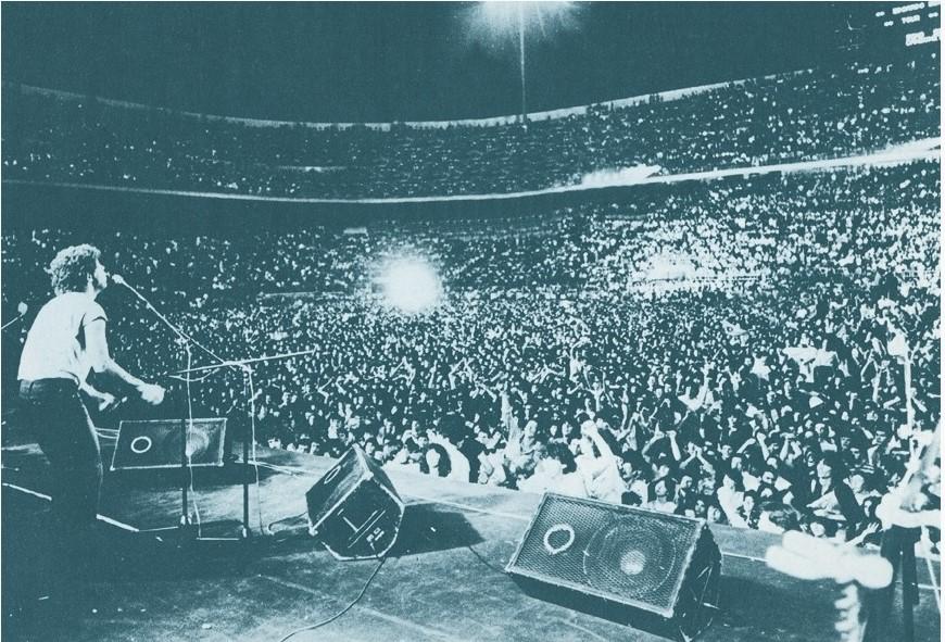 San Siro, 19 July 1980 — Edoardo Bennato plays to an ocean of Milanese in the stadium's first great rock concert. It is the exact summer of the fall: between the Totonero sentence of the spring and the first Serie B kick-off of September, this is how the cathedral of Milanese football filled its silence.