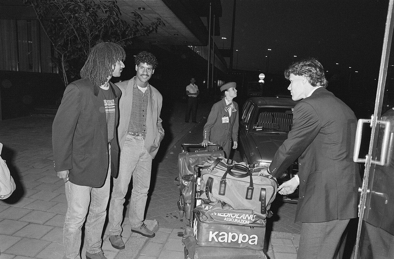 Ruud Gullit, Frank Rijkaard and Marco van Basten arrive in the Netherlands on 28 May 1989 — four days after the Camp Nou night when Milan destroyed Steaua Bucuresti 4-0, Gullit and Van Basten scoring two apiece. On the trolley, the club's Kappa and Mediolanum Assicurazioni bags: Europe's new champions travelling with Berlusconi's name on their luggage.
