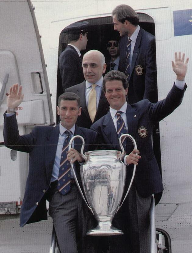 Mauro Tassotti, Fabio Capello and Adriano Galliani with the Champions League trophy on the squad's return to Italy after the 4-0 demolition of Barcelona in Athens on 18 May 1994 — goalkeeper Sebastiano Rossi visible behind them. Capello's third trophy in his third season, won without Baresi and Costacurta, both suspended.
