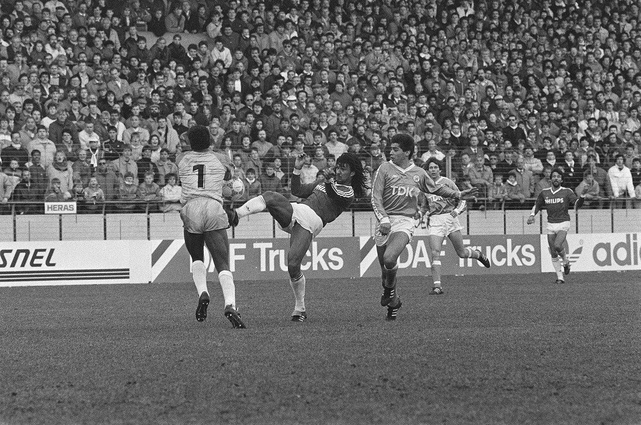 Ruud Gullit, in PSV's dark Philips shirt, hooks the ball clear of Ajax goalkeeper Stanley Menzo in Eindhoven, 29 March 1987 — the first full season of Berlusconi's presidency. Milan's emissaries were already fixed on the dreadlocked totem of Dutch football; within months a world-record fee would carry him to Milanello.