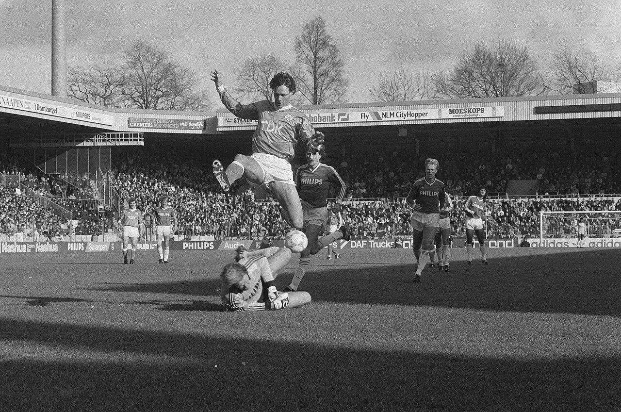 Marco van Basten, in Ajax's TDK shirt, hurdles PSV goalkeeper Hans van Breukelen — same afternoon in Eindhoven, 29 March 1987, minutes from Gullit's duel at the other end. Back from the December ankle operation and already promised to Milan, the two Dutchmen who would define the Berlusconi era shared one frame of Dutch football before boarding for Italy.